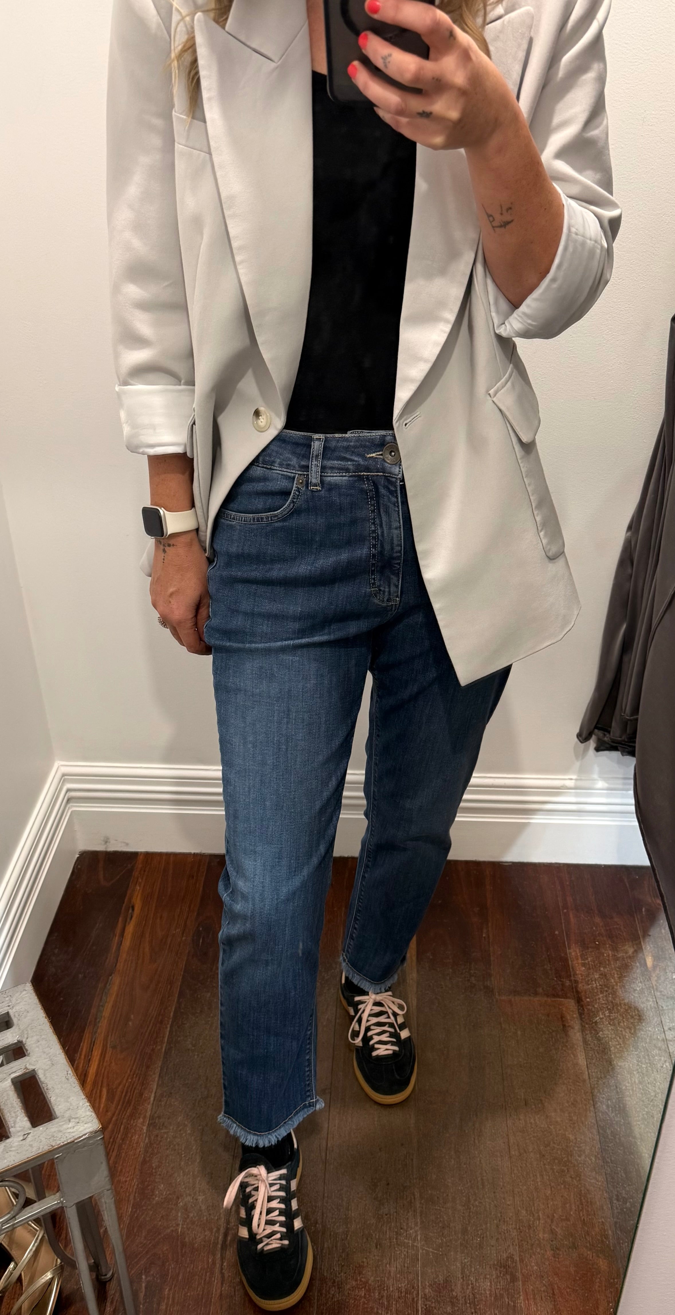 Person wearing a light gray blazer, black shirt, blue jeans, and black sneakers in a mirror reflection.