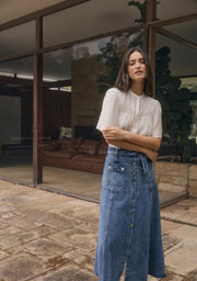 Mos the Label Aveline Denim Midi Skirt in light wash, featuring a fitted waist and flowing silhouette, displayed on a hanger.